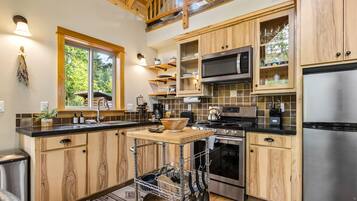 A modern kitchen with wooden cabinets, stainless steel appliances, and a window overlooking greenery.