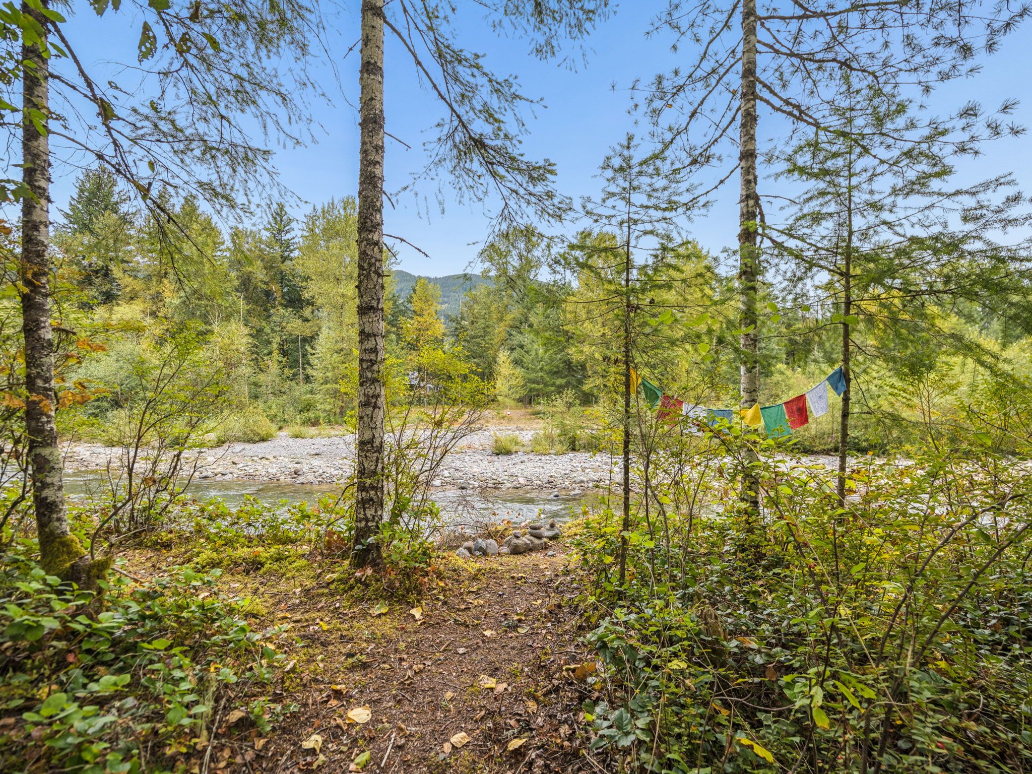 A natural landscape with a river, trees, and a prayer flag.