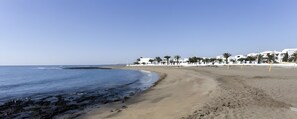 A beach with a clear sky, a sandy shore, and white buildings with palm trees. - Vacation Apartment 'Playa Honda' with Private Terrace and Wi-Fi (Playa Honda)