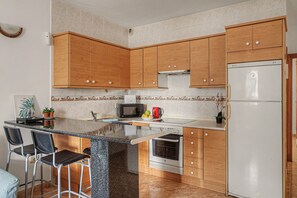 A kitchen with wooden cabinets, a microwave, a kettle, and a refrigerator. - Vacation Apartment 'Playa Honda' with Private Terrace and Wi-Fi (Playa Honda)