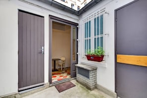 A narrow entrance with a closed door, a small table with a chair, and a window with a plant. - Studio Apartment for 2 People - Voltaire - Père Lachaise - Paris 11th - Modern (Paris)