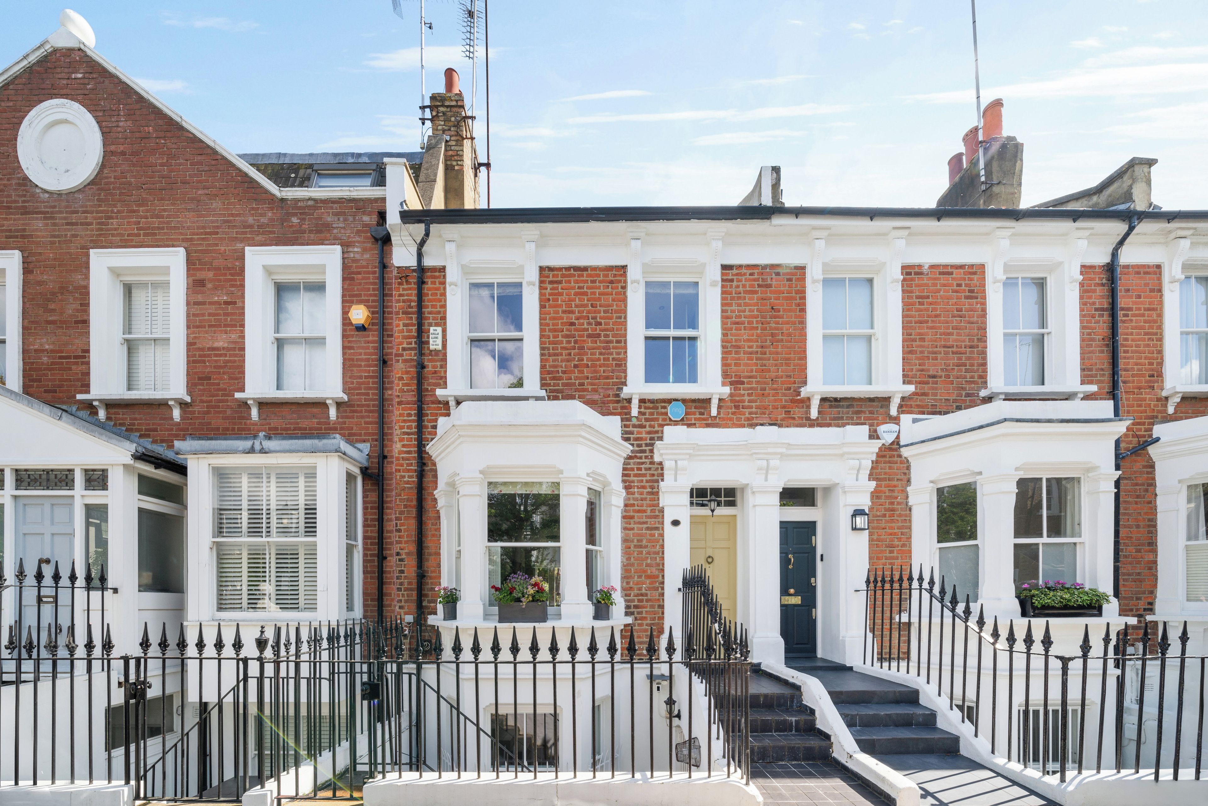 A row of terraced houses with white front doors, black iron railings, and a clear blue sky.