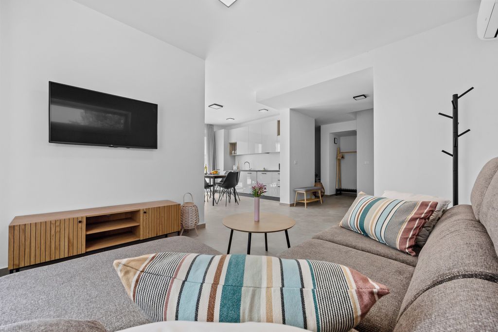 Una sala moderna con televisor de pantalla plana, un mueble bajo de madera, una mesa de centro redonda y un sofá con cojines a rayas.