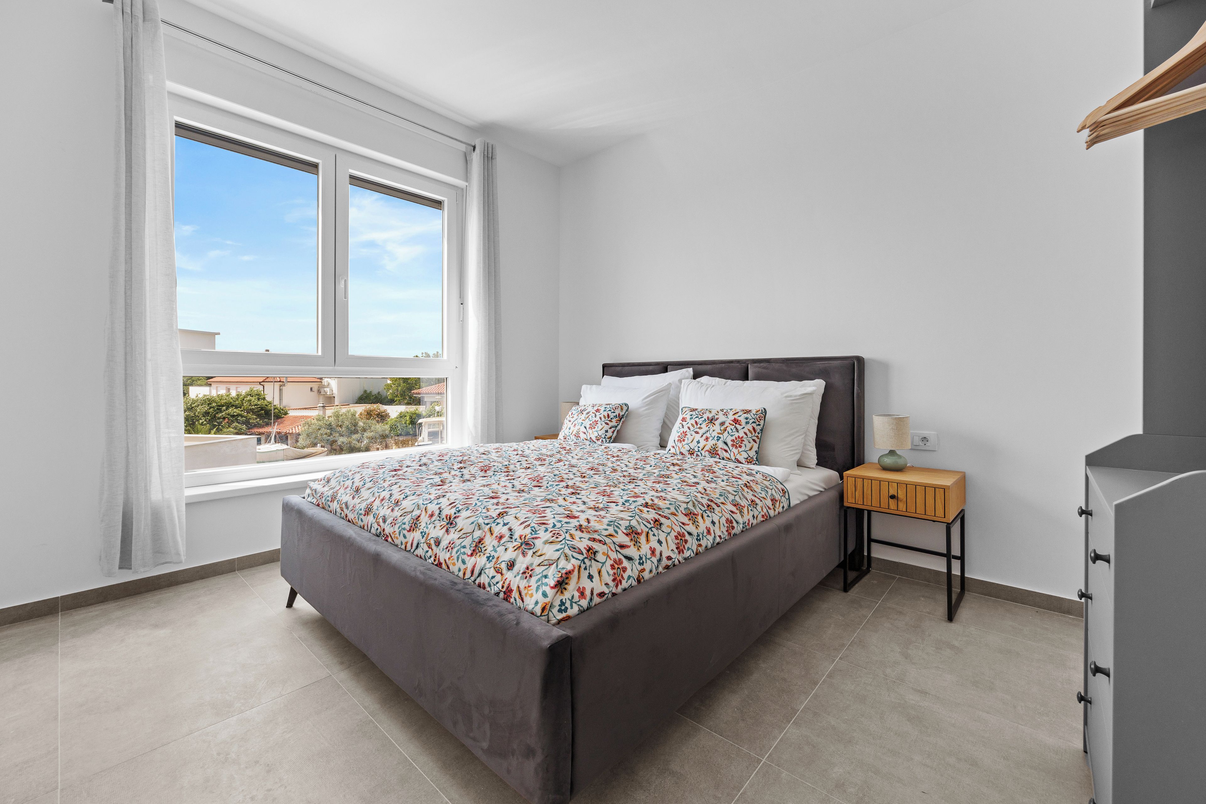 A modern bedroom with a large bed, a bedside table with a lamp, and a view of the outside.