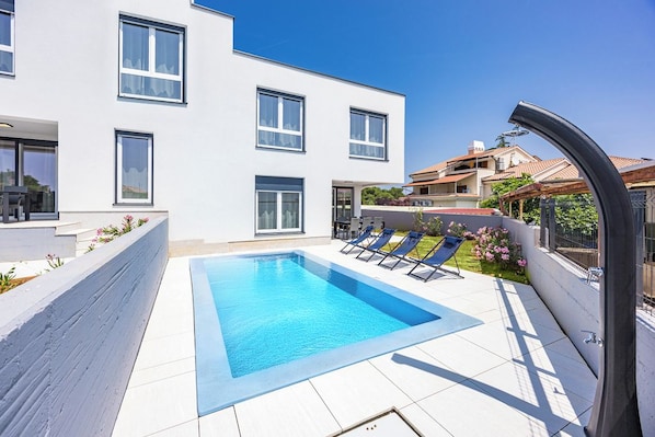 Un bâtiment moderne doté d’une piscine, de chaises longues et offrant une vue sur un ciel dégagé.