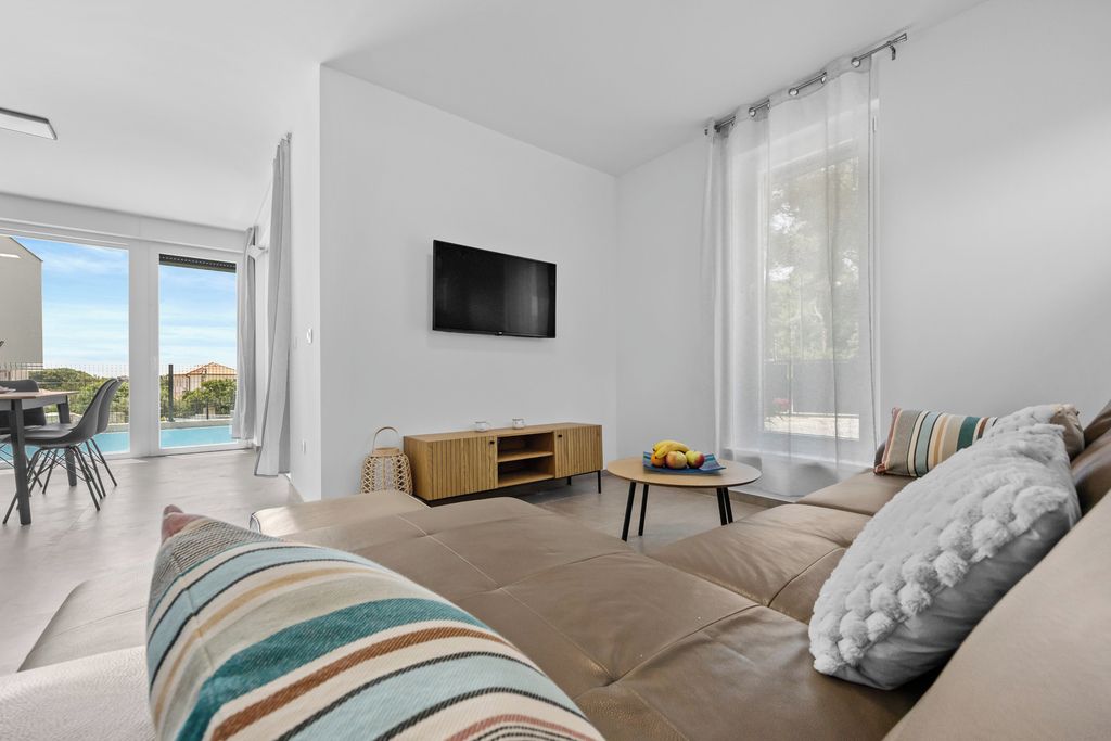 Una sala de estar moderna con un sofá, un televisor instalado en la pared y un comedor con mesa y sillas.