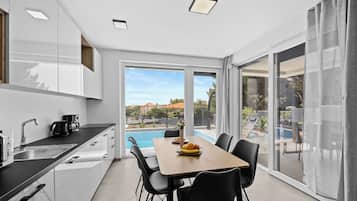 Una cocina moderna con comedor, vista a la piscina y puerta corrediza de vidrio que da a un área de estar exterior.