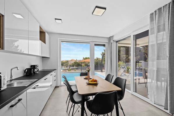 A modern kitchen with a dining area, a pool view, and a sliding glass door leading to an outdoor seating area.