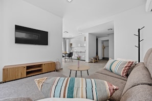Un salon moderne avec un téléviseur à écran plat, un canapé avec des coussins à rayures, une table basse et un coin repas à l’arrière-plan.