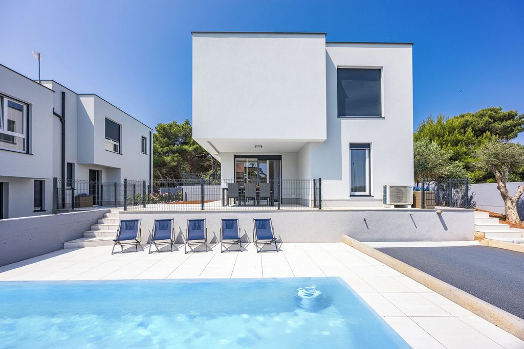Un edificio moderno de dos pisos con piscina y sillones de descanso.