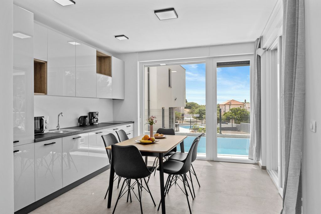 A modern kitchen with a dining area, large windows, and a view of a swimming pool.
