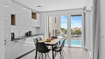 A modern kitchen with a dining area, large windows, and a view of a swimming pool.