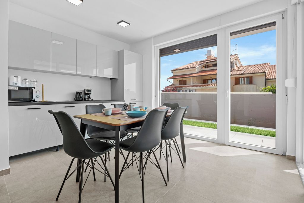 Cocina moderna con armarios blancos, una mesa de comedor con sillas y vistas a una zona residencial a través de grandes puertas corredizas de vidrio.