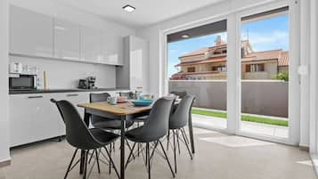 Cocina moderna con armarios blancos, una mesa de comedor con sillas y vistas a una zona residencial a través de grandes puertas corredizas de vidrio.