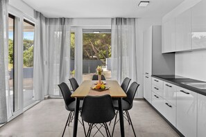 Une cuisine moderne avec une table et des chaises, une grande fenêtre avec des rideaux et une vue sur la verdure à l’extérieur.
