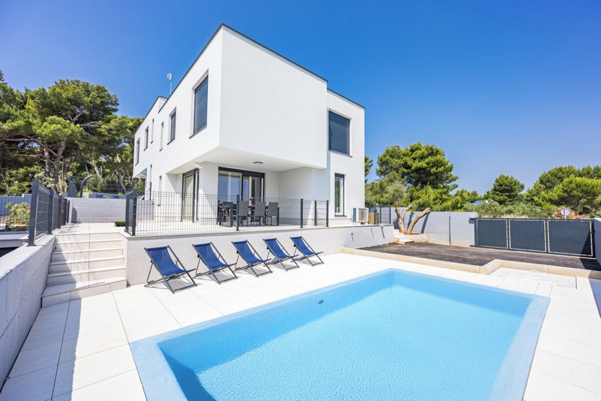 A modern two-story house with a swimming pool, outdoor seating, and a clear sky.