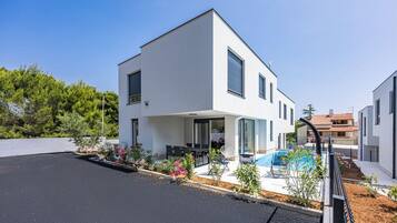 A modern two-story house with a swimming pool, outdoor seating, and a well-maintained garden.