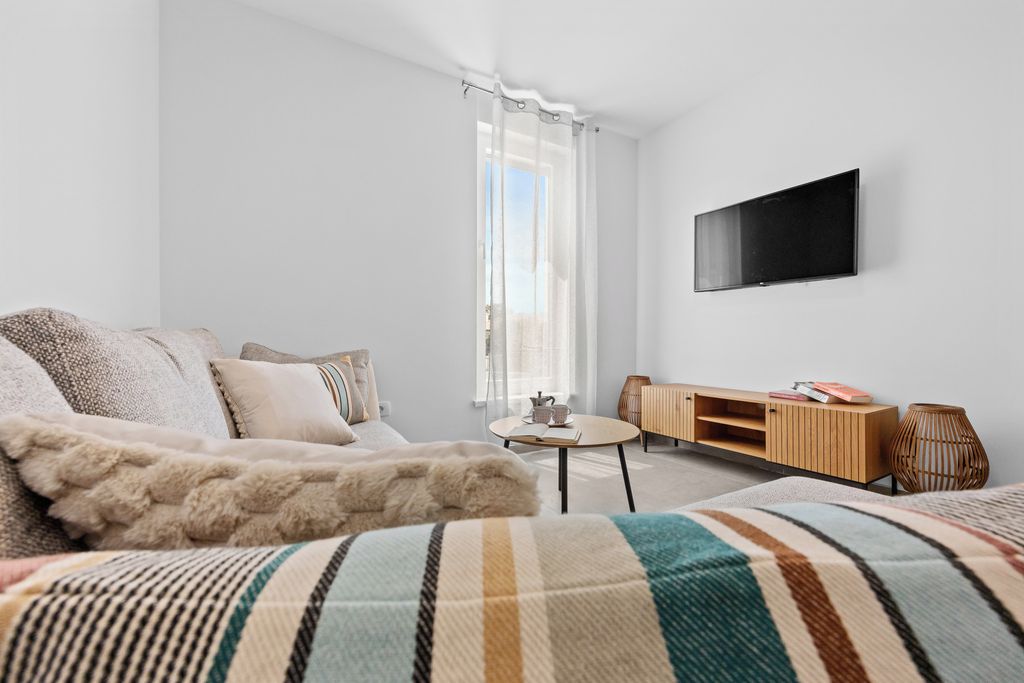 Ein modernes Wohnzimmer mit einer Couch, einem Couchtisch und einem an der Wand befestigten Fernseher.