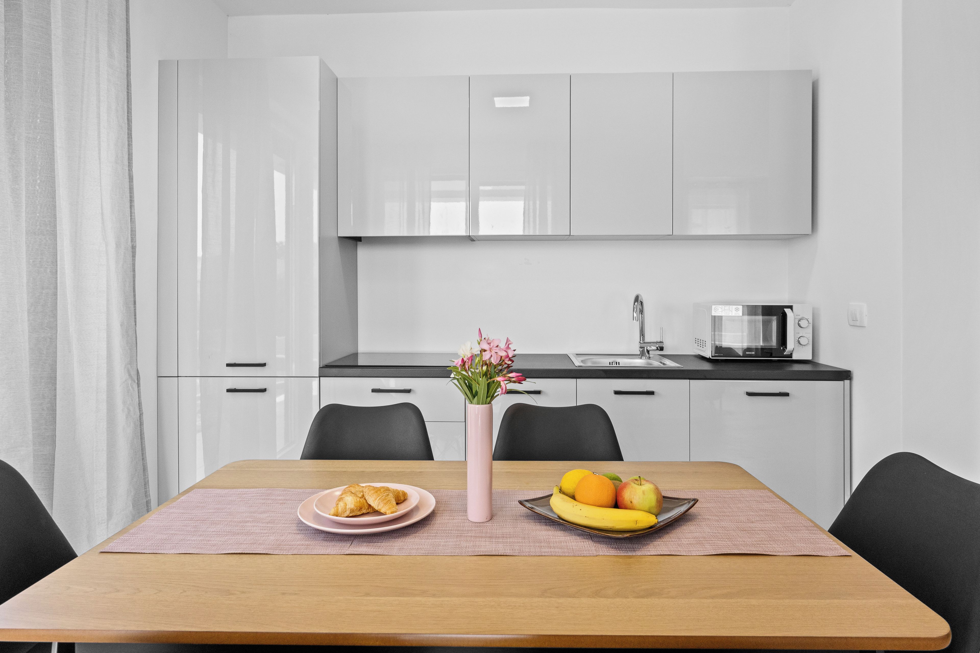 Una cocina moderna con armarios blancos, encimera negra y una zona de comedor con una mesa dispuesta para dos.