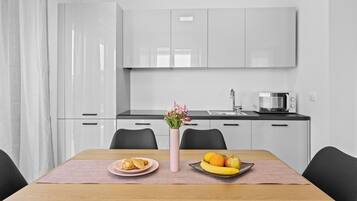 Una cocina moderna con armarios blancos, encimera negra y una zona de comedor con una mesa dispuesta para dos.