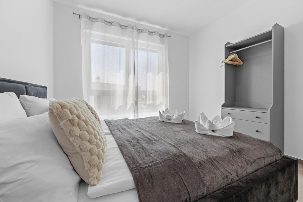 A modern bedroom with a bed, a wardrobe, and a window with sheer curtains.