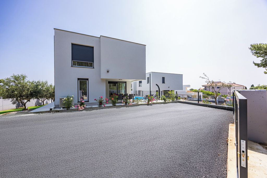 A modern two-story building with a flat roof, a large window on the ground floor, and a small balcony.