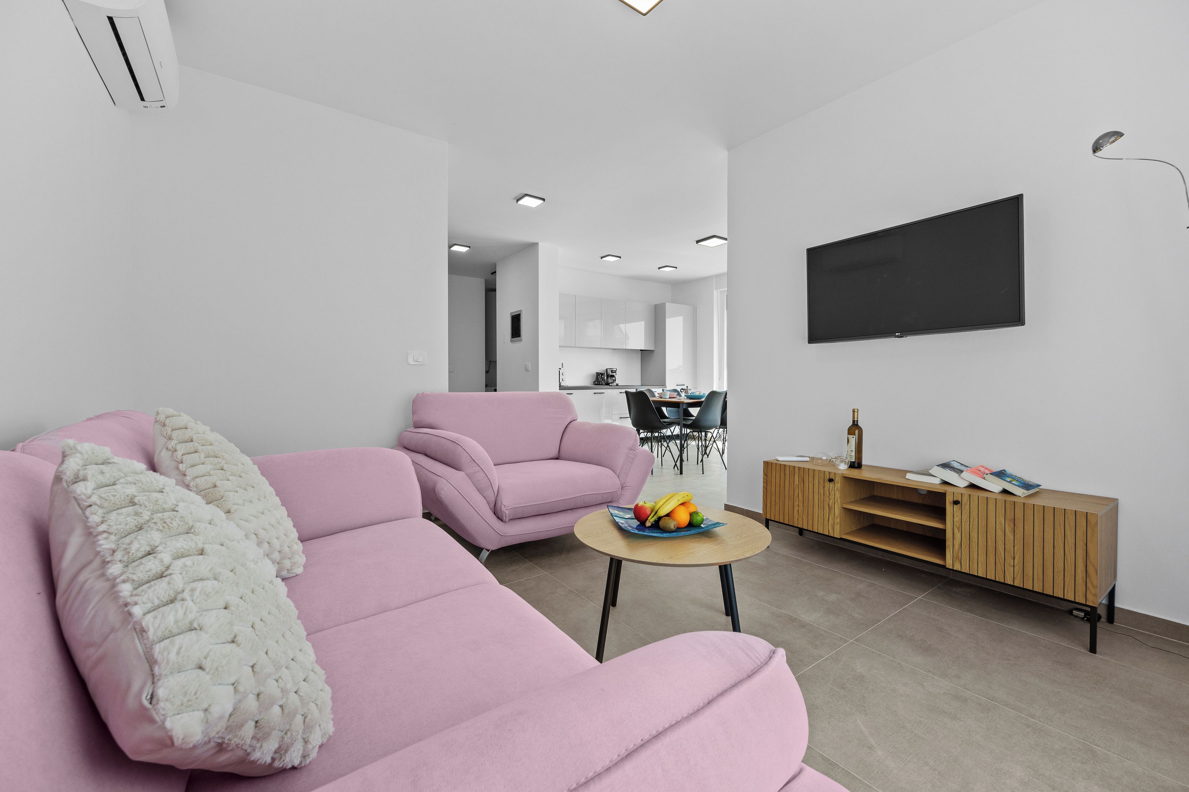 Una sala de estar moderna con un sofá rosa, una mesita redonda con fruta y un mueble de entretenimiento de madera.