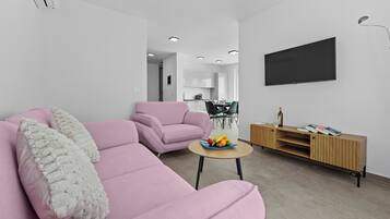 Una sala de estar moderna con un sofá rosa, una mesita redonda con fruta y un mueble de entretenimiento de madera.