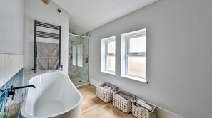 Un baño moderno con una bañera independiente, cabina de ducha con mampara de vidrio y una ventana con persianas.