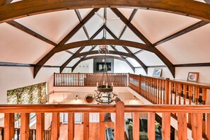 A spacious interior with a high ceiling, wooden beams, a central chandelier, and a staircase with wooden railings. - Grenville House (Kilkhampton)