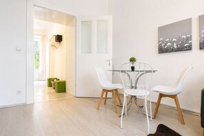 A modern dining area with a glass table, white chairs, and a green accent chair. - Belvedere on Foot Your Vienna 1BR (Vienna)