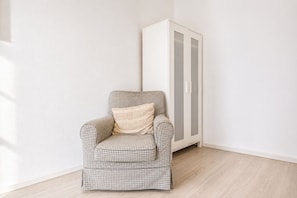 A checkered armchair with a cushion in a corner of a room with a white wardrobe and light wooden flooring. - Belvedere on Foot Your Vienna 1BR (Vienna)