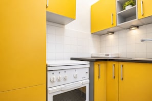 A kitchen with yellow cabinets, a white stove, and a white tiled backsplash. - Belvedere on Foot Your Vienna 1BR (Vienna)