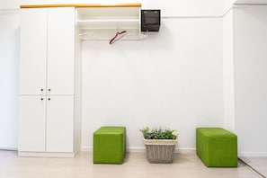 A room with a white wardrobe, a small shelf with a black object, and two green stools. - Belvedere on Foot Your Vienna 1BR (Vienna)