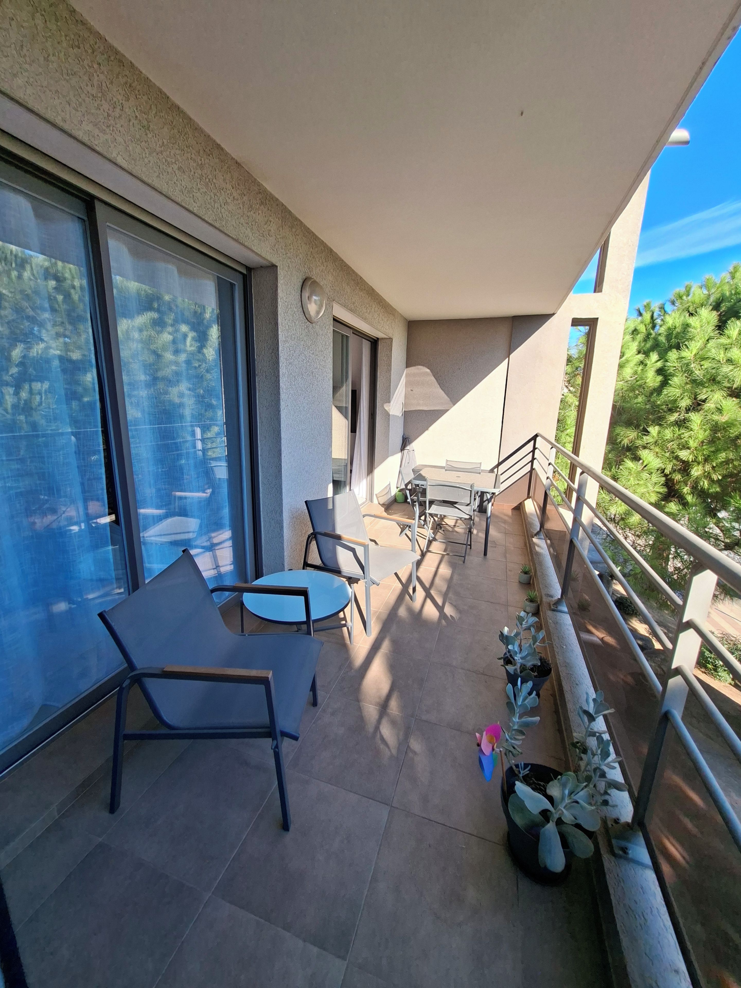 A balcony with seating, a table, and potted plants.