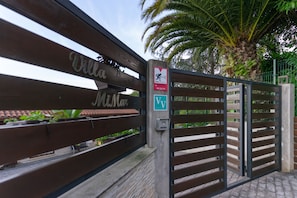 A gated entrance with a sign that reads 'Villa McNair' and a security warning sign.