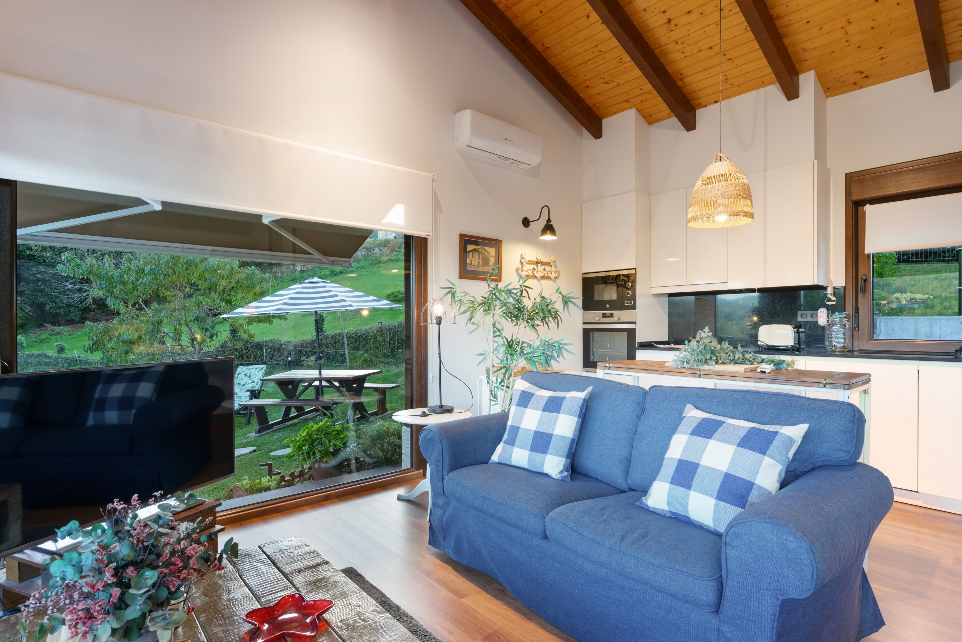Una sala de estar moderna con un ventanal grande, un sofá azul y vistas a un jardín.