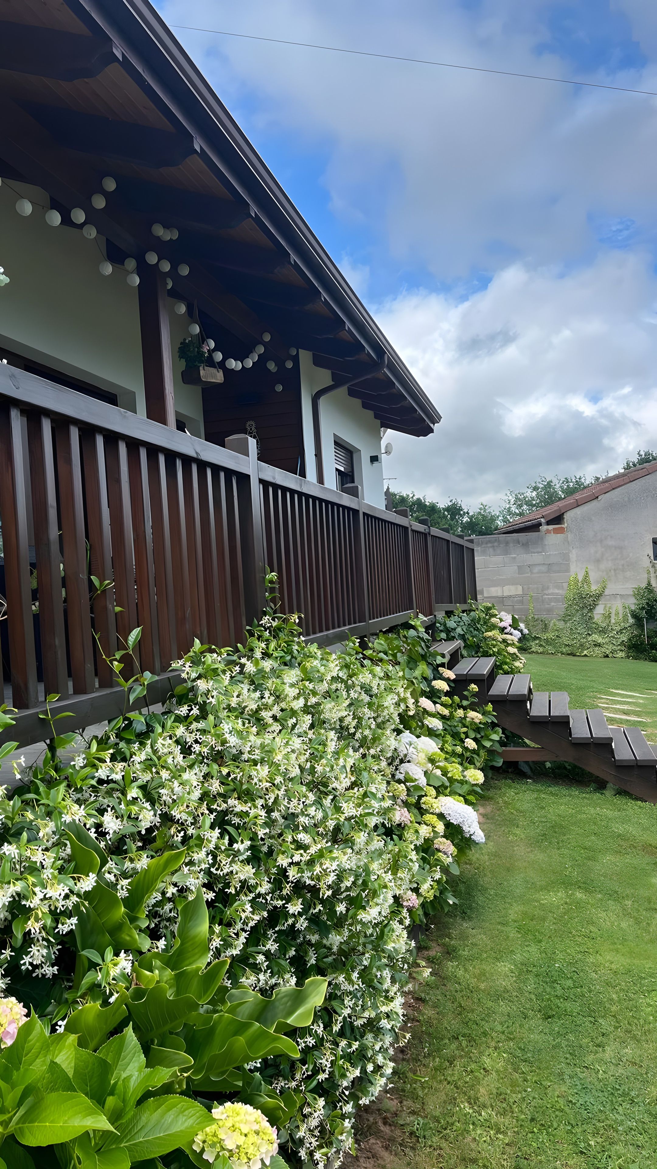 En bygning med træterrasse, græsplæne og mange forskellige planter.