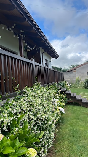 A building with a wooden deck, a grassy yard, and a variety of plants.