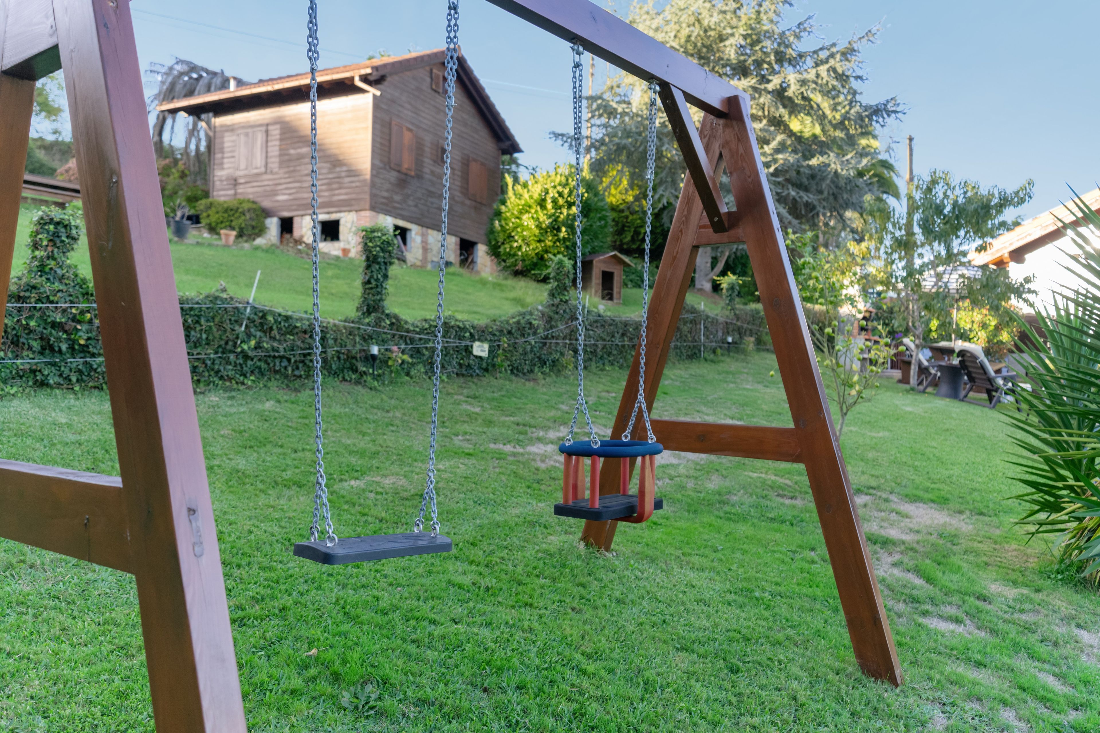 Un ensemble de balançoires en bois installé dans une cour verdoyante, avec une maison en arrière-plan.