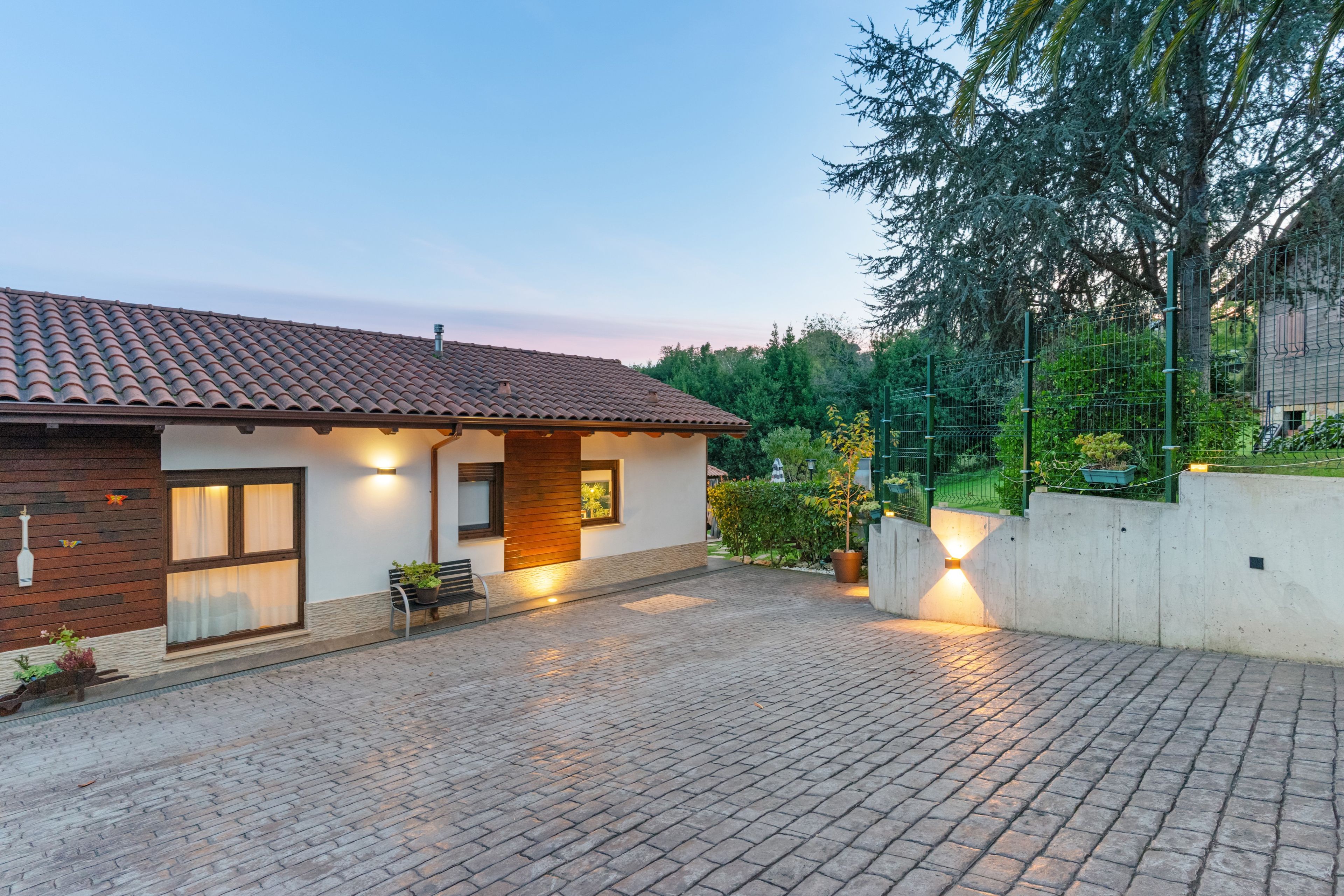 Une maison avec un toit en tuiles, une allée pavée et un jardin clos.