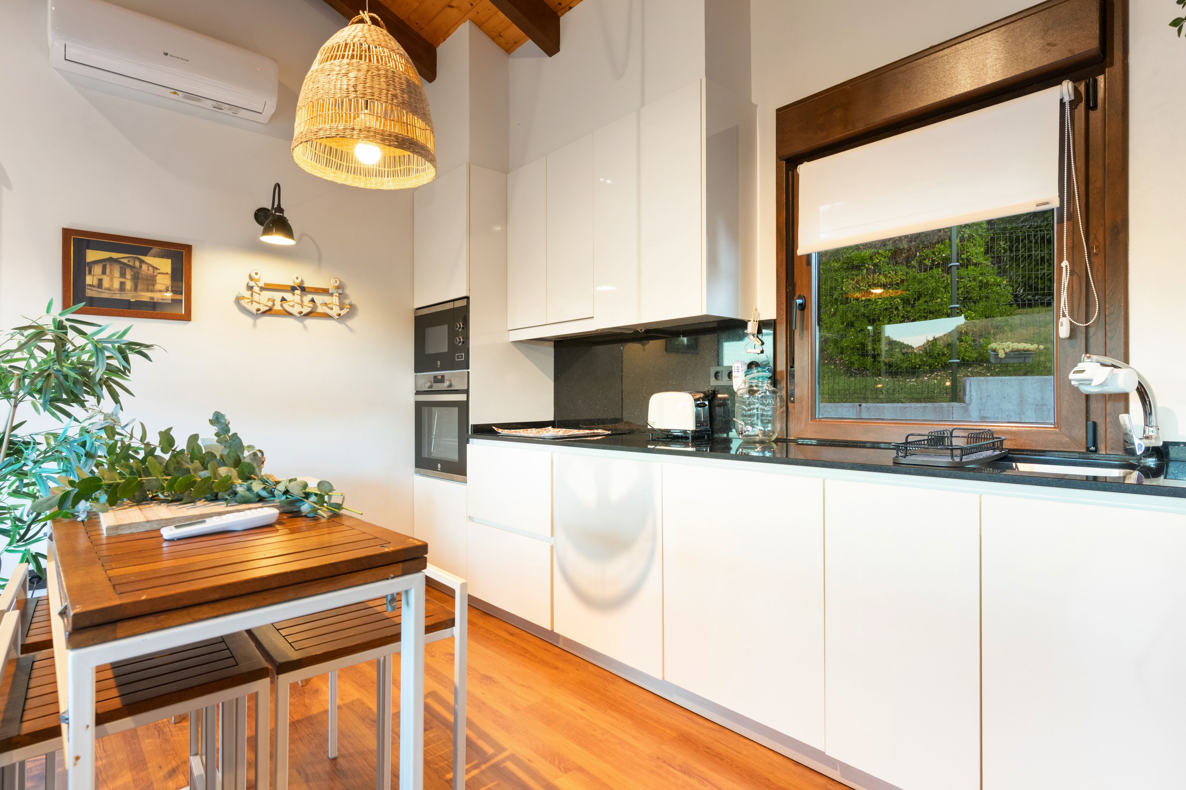 Una cocina moderna con armarios blancos, una mesa de comedor de madera y una lámpara colgante.