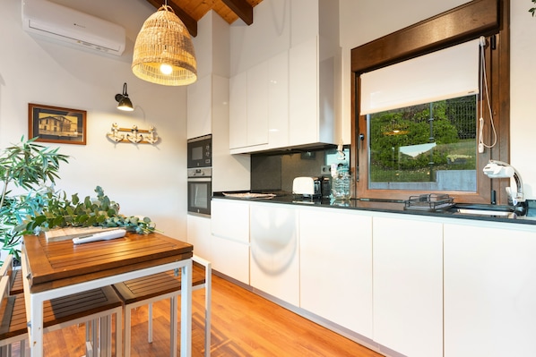 A modern kitchen with white cabinets, a wooden dining table, and a hanging light fixture.