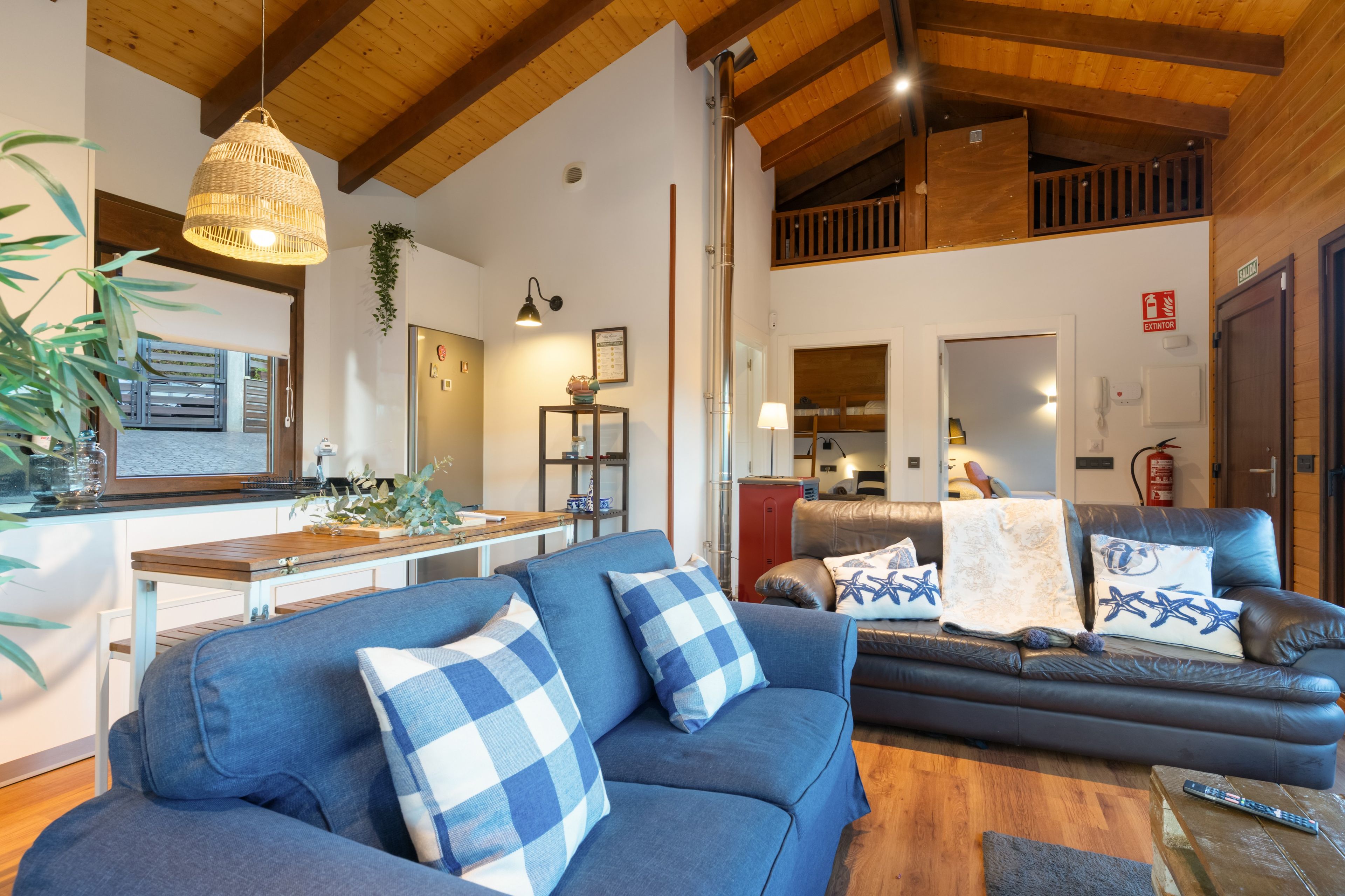 Ein modernes Wohnzimmer mit einem blauen Sofa, einer Holzzieldecke und einem Küchenbereich im Hintergrund.