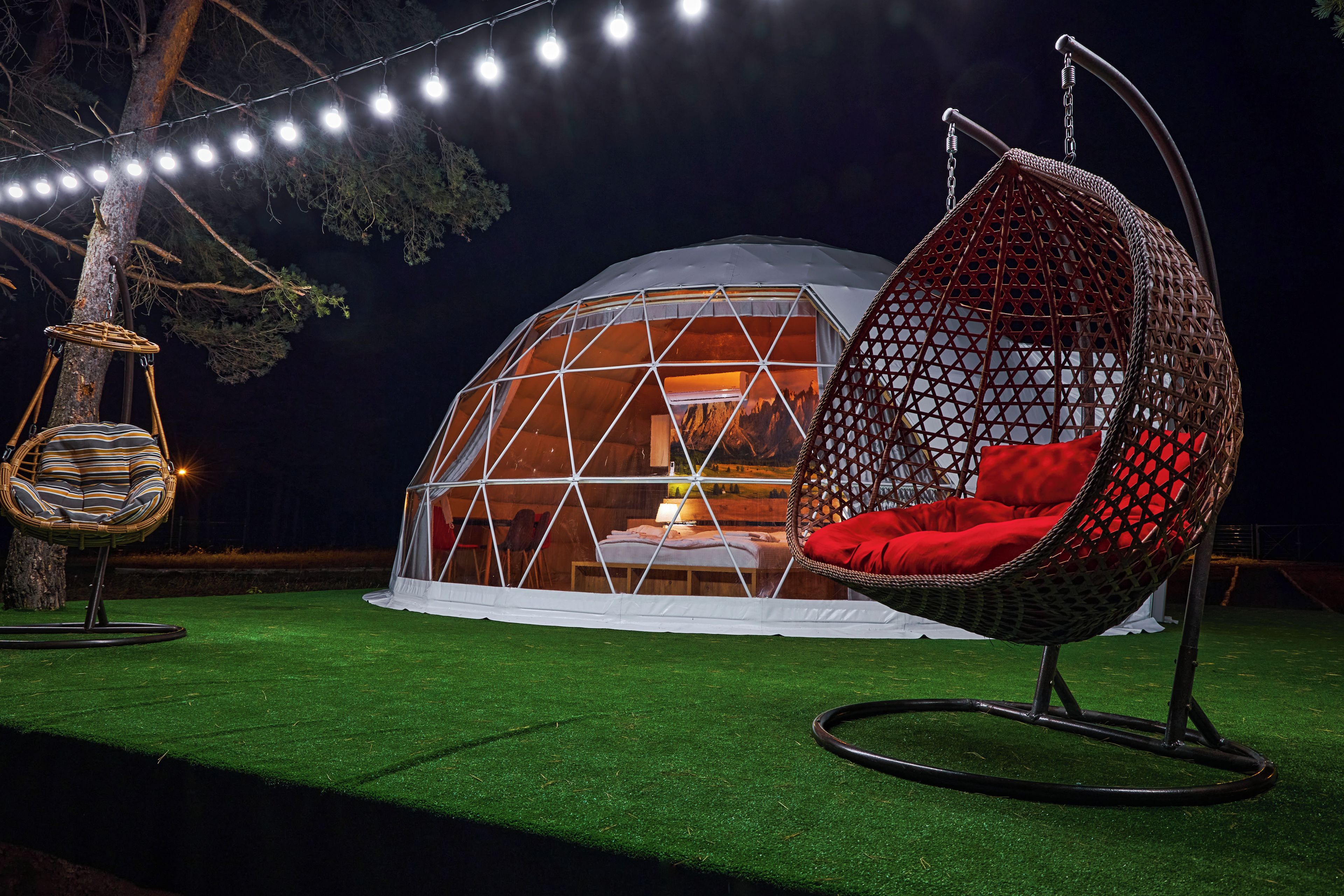 Una tienda en forma de domo geodésico con una silla colgante y un columpio en el exterior.