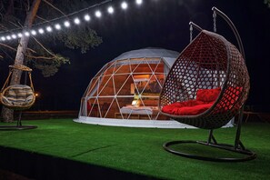 A geodesic dome tent with a hanging chair and a swing chair outside.