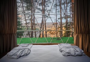 Un letto con lenzuola e asciugamani bianchi, una finestra vista su una foresta e un'altalena.