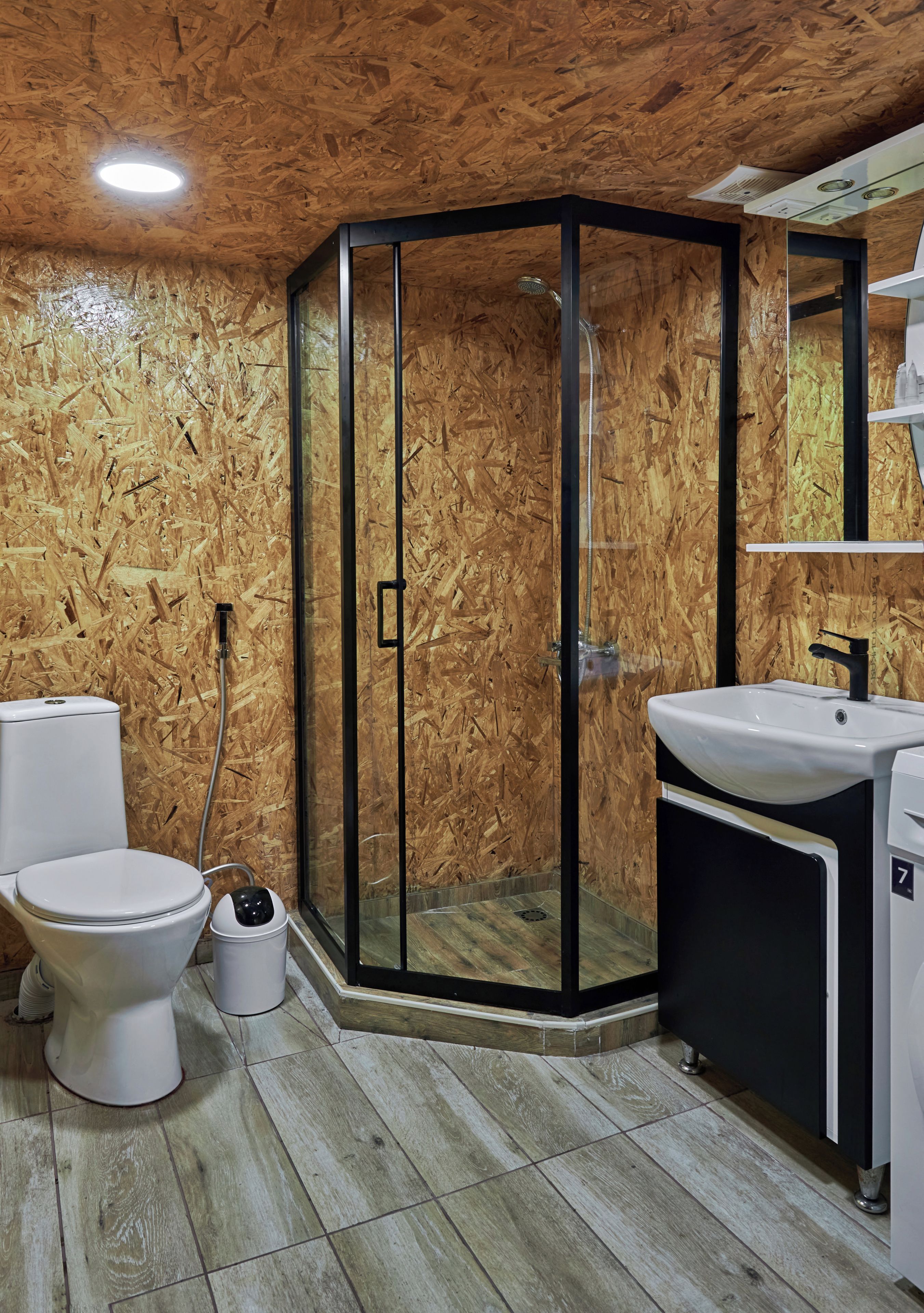 Un baño con pared de madera, cabina de ducha de cristal, inodoro, lavamanos y espejo.