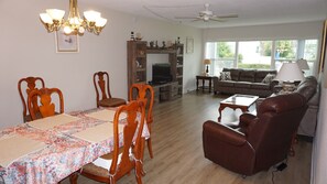 Una sala de estar con una mesa de comedor, sillas, un sofá, una mesa de centro, un televisor y un ventilador de techo.