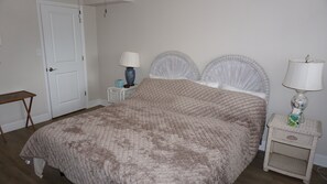 Un dormitorio con cama, mesitas de noche, una puerta y una pequeña mesa.
